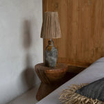 Nestled corner of a bedroom with a wooden side table and lamp against a wooden wall.