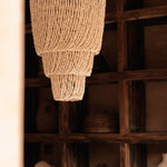 Woven chandelier hanging in a rustic interior setting with wooden shelves.