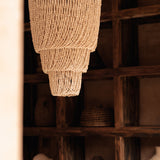 Woven chandelier hanging in a rustic interior setting with wooden shelves.