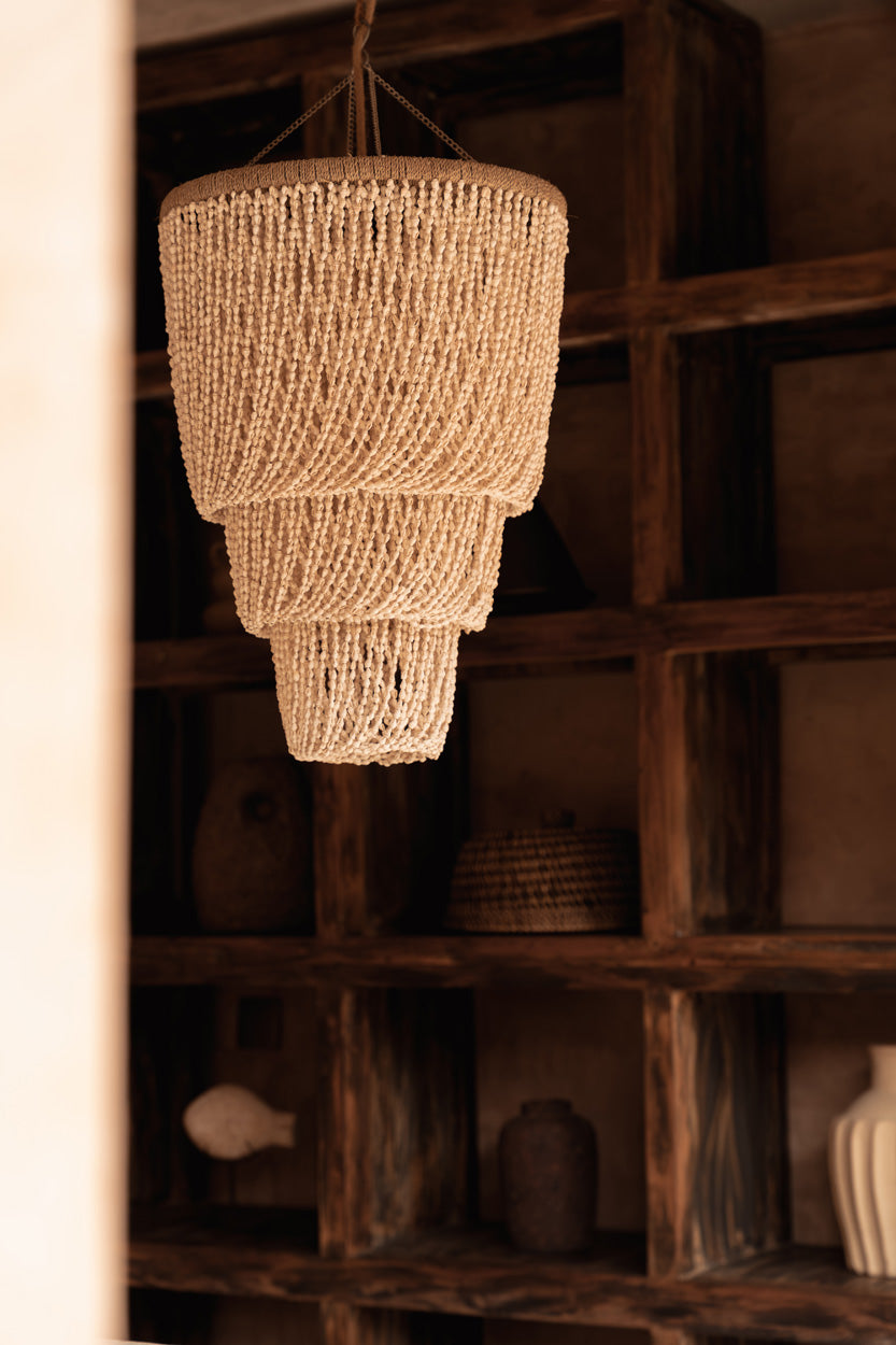 Woven chandelier hanging in a rustic interior setting with wooden shelves.