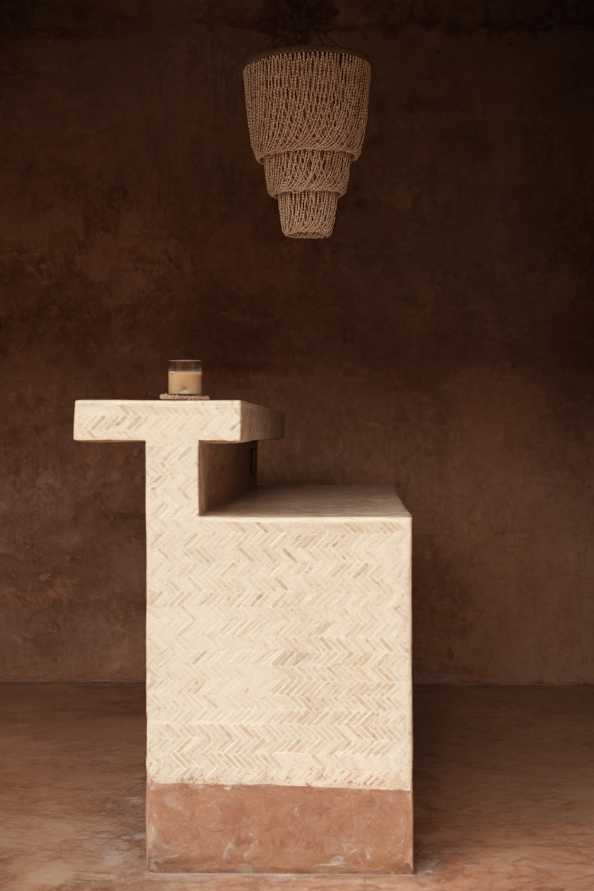 Textured stone pedestal with a hanging shell chandelier light on a brown background