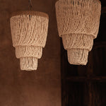 Two layered beaded shell pendant light chandeliers hanging against a brown wall.