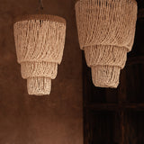 Two layered beaded shell pendant light chandeliers hanging against a brown wall.