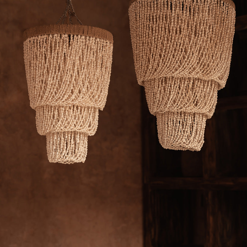 Two layered beaded shell pendant light chandeliers hanging against a brown wall.