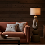 Cosy living room with a brown sofa, decorative pillows, a  neutral floor lamp, and wooden wall.