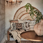 Modern rustic boho  indoor setting with a wicker chair, patterned cushions, and a rough plaster wall.