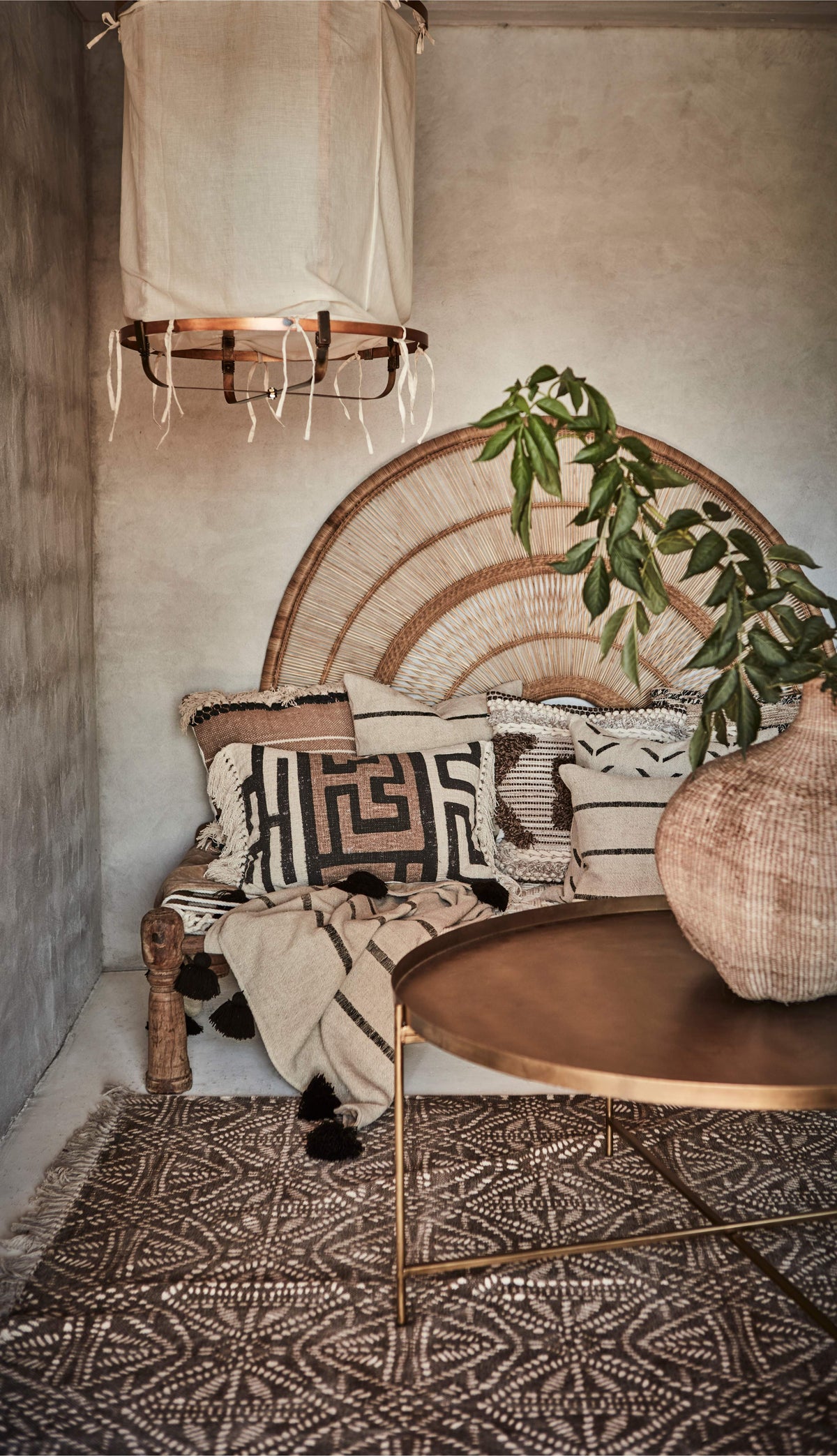 Modern rustic boho  indoor setting with a wicker chair, patterned cushions, and a rough plaster wall.