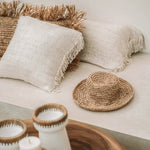 Decorative setting with woven raffia, candles, and cushions on a neutral sofa