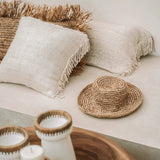 Decorative setting with woven raffia, candles, and cushions on a neutral sofa