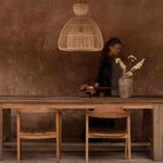 Wooden dining table with large rattan light shade with chairs against a textured brown wall.