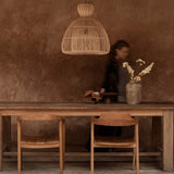 Wooden dining table with large rattan light shade with chairs against a textured brown wall.