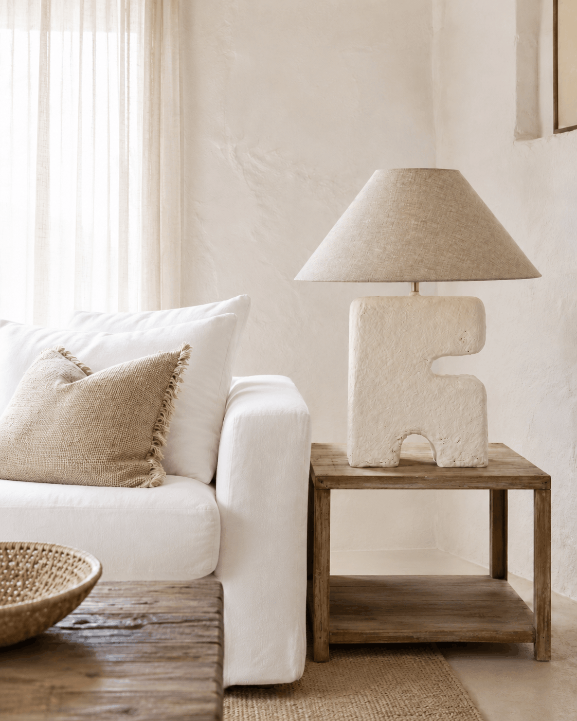 Large architectural table lamp on wooden shelved side table and cream beige sofa