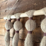 Close-up of a wooden wall hanging  with tassels on a rustic wooden wall