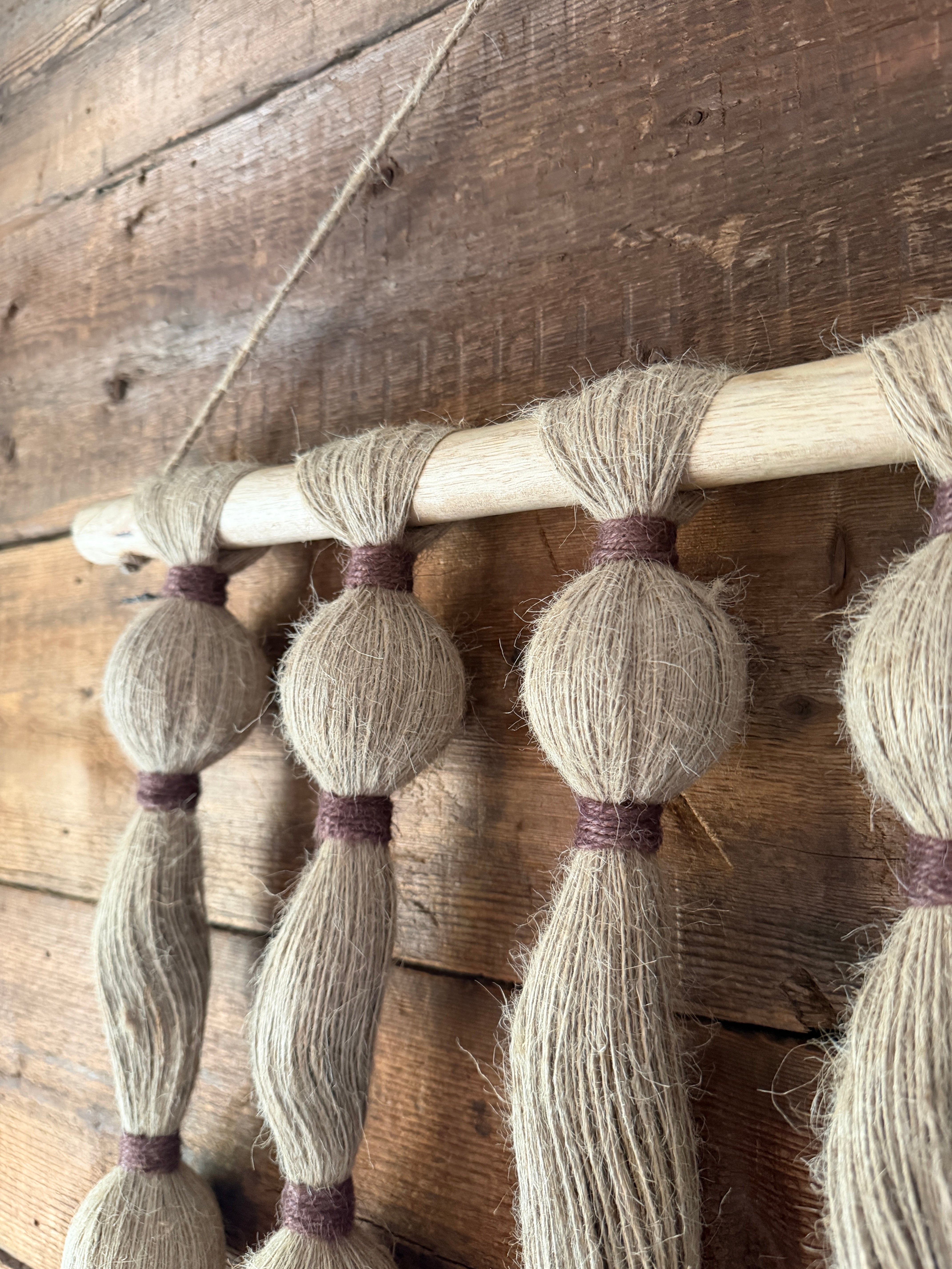 Close-up of a wooden wall hanging  with tassels on a rustic wooden wall