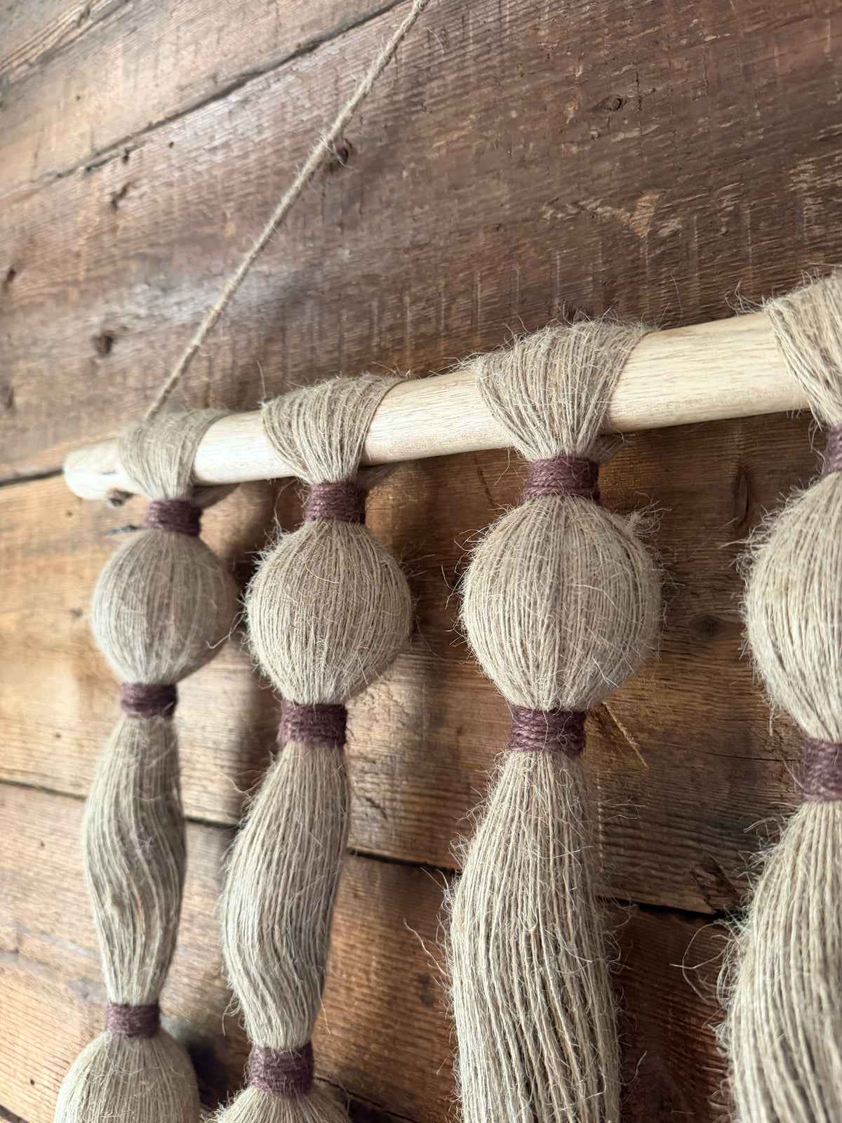 Close up of a wooden wall hanging  with tassels on a rustic wooden wall