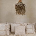 Textured cushions on a sofa with a woven rattan natural pendant light against a beige wall.