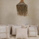 Textured cushions on a sofa with a woven rattan natural pendant light against a beige wall.