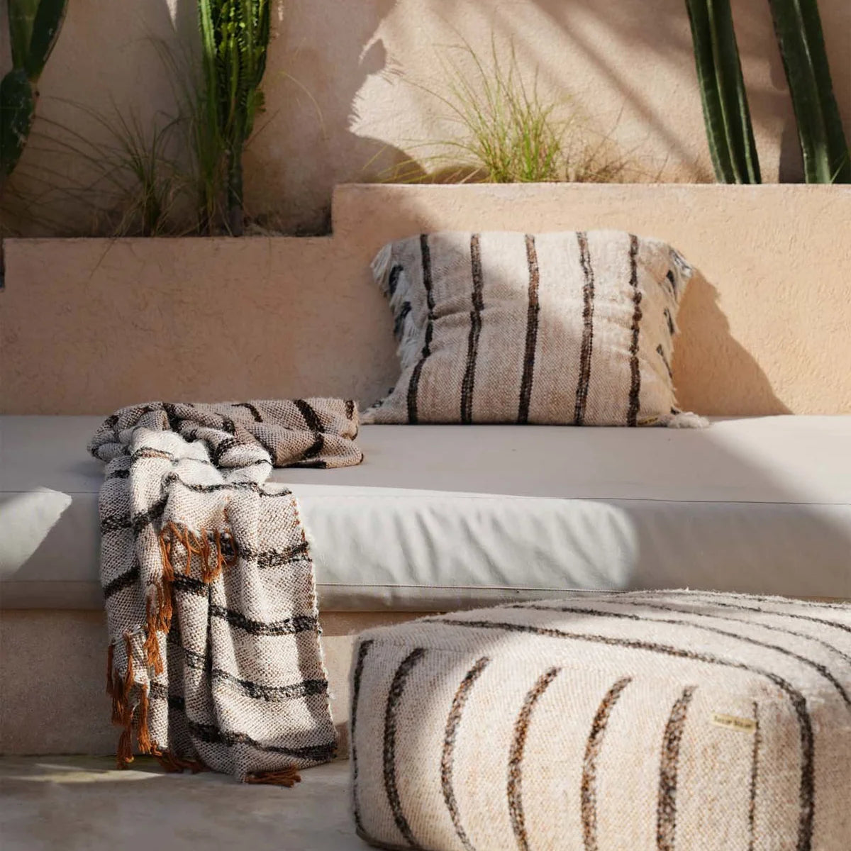 Outdoor seating area with striped cushions and a blanket, surrounded by cacti.
