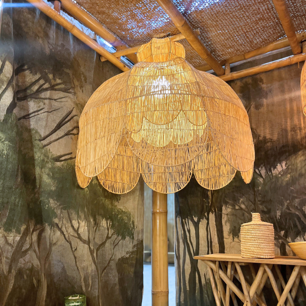 Woven raffia, rattan lampshade hanging from a bamboo structure with a forest mural in the background