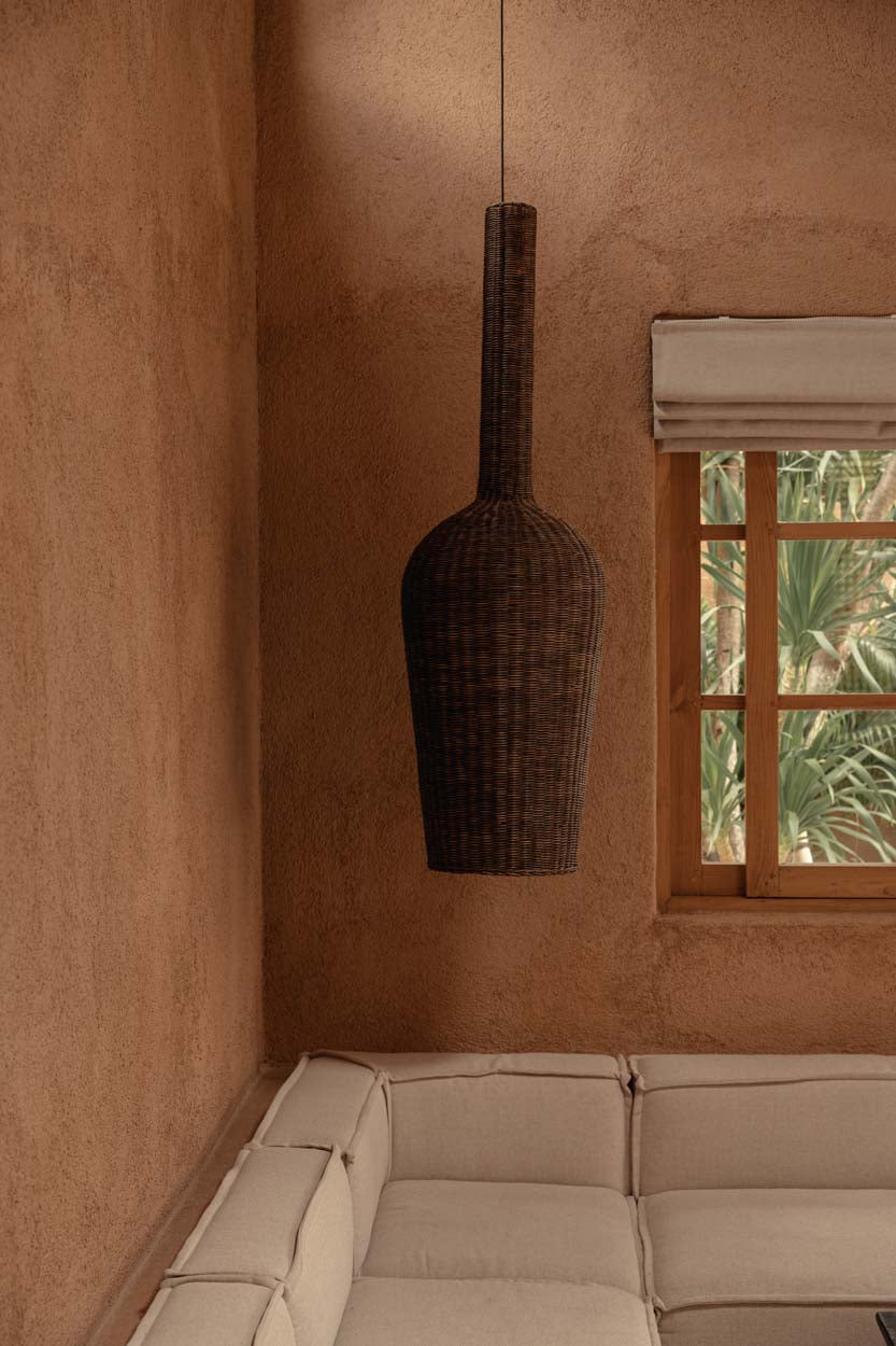 Woven dark rattan pendant light hanging above a beige sofa against a textured wall with a window.
