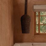 Woven dark rattan pendant light hanging above a beige sofa against a textured wall with a window.