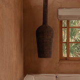 Woven dark rattan pendant light hanging above a beige sofa against a textured wall with a window.
