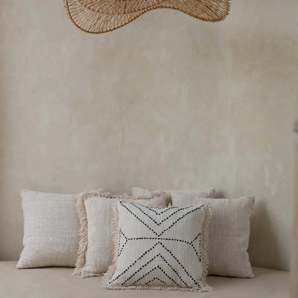 Decorative pillows on a bed with a large woven rattan flat pendant light fixture above.