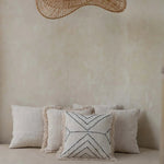 Decorative pillows on a bed with a large woven rattan flat pendant light fixture above.
