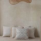 Decorative pillows on a bed with a large woven rattan flat pendant light fixture above.