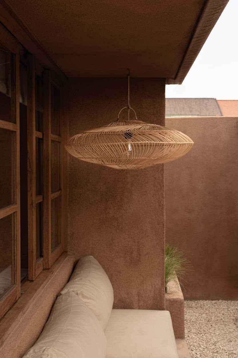 Woven rattan pendant light hanging in a room with a plastered wall and conservatory