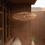 Woven rattan pendant light hanging in a room with a plastered wall and conservatory