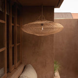 Woven rattan pendant light hanging in a room with a plastered wall and conservatory
