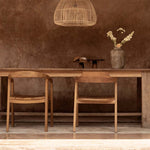large rattan pendant light above a Wooden dining table with chairs against a textured brown wall.