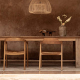 large rattan pendant light above a Wooden dining table with chairs against a textured brown wall.