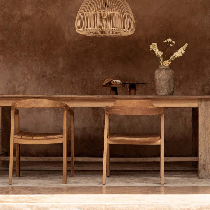 large rattan pendant light above a Wooden dining table with chairs against a textured brown wall.