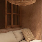 Beige sofa with textured pillow under a large wicker rattan pendant lime wash walls