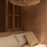 Beige sofa with textured pillow under a large wicker rattan pendant lime wash walls