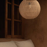 Woven rattan round pendant light hanging above a sofa with a wooden shelf in the background.