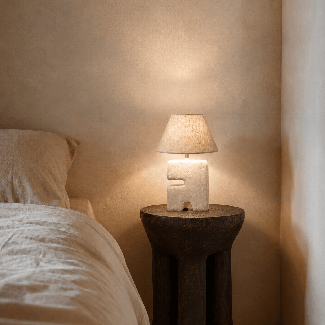 Bedside , space saving small Lamp on a wooden side table next to a bed in a softly lit room