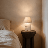 Bedside , space saving small Lamp on a wooden side table next to a bed in a softly lit room