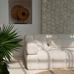 White sofa in a room with a stone wall and plant with ivory cream tasselled cushion covers