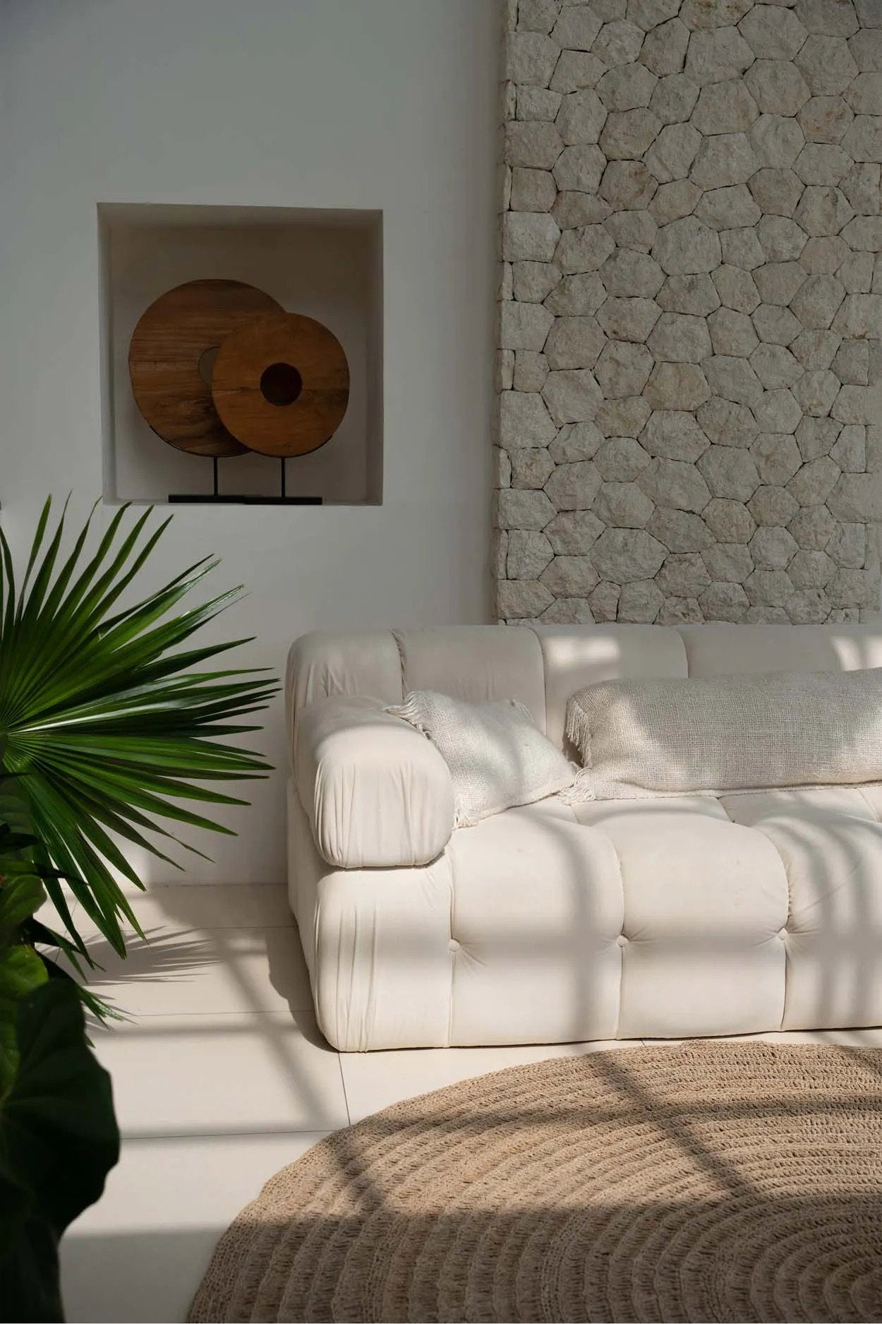 White sofa in a room with a stone wall and plant with ivory cream tasselled cushion covers