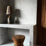 Wooden stool and raffia table  lamp on a concrete surface with a textured wall background