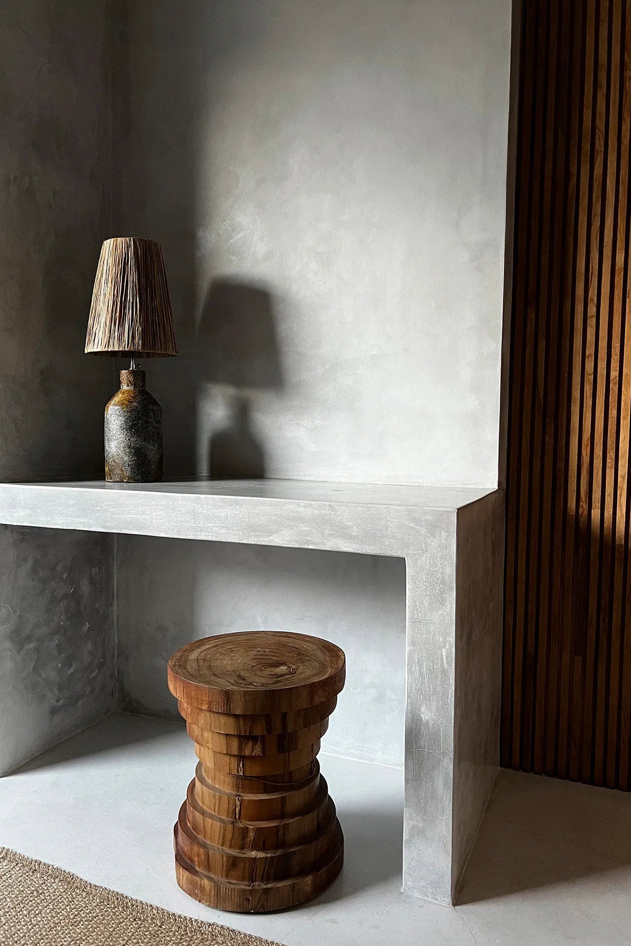 Wooden stool and raffia table  lamp on a concrete surface with a textured wall background