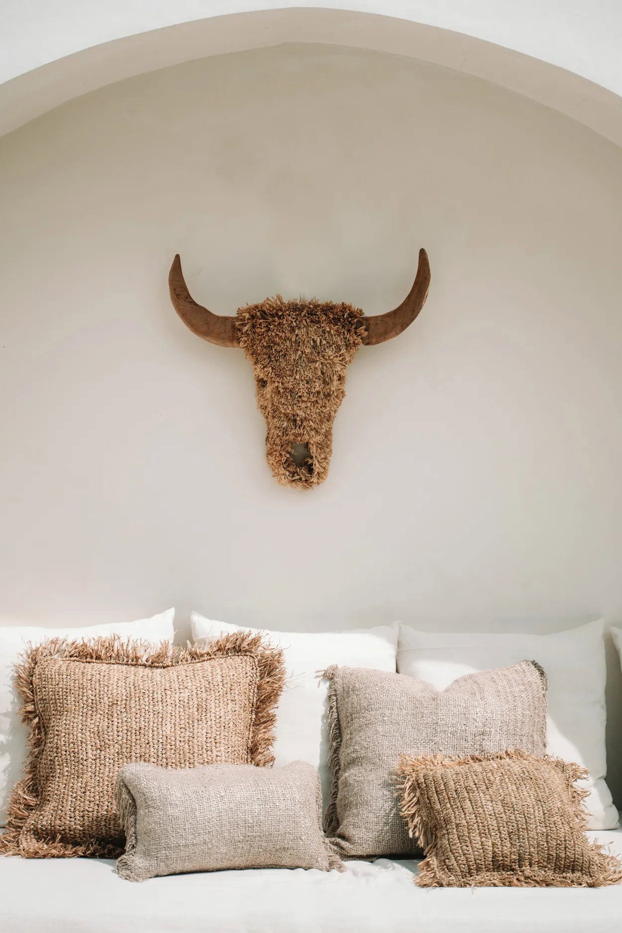 Decorative pillows on a sofa with a bull head sculpture on the wall.