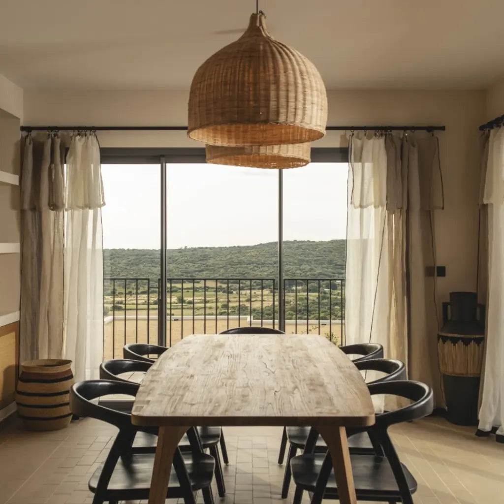large light rattan wicker dome light shade hanging over long wood dining table in rustic room
