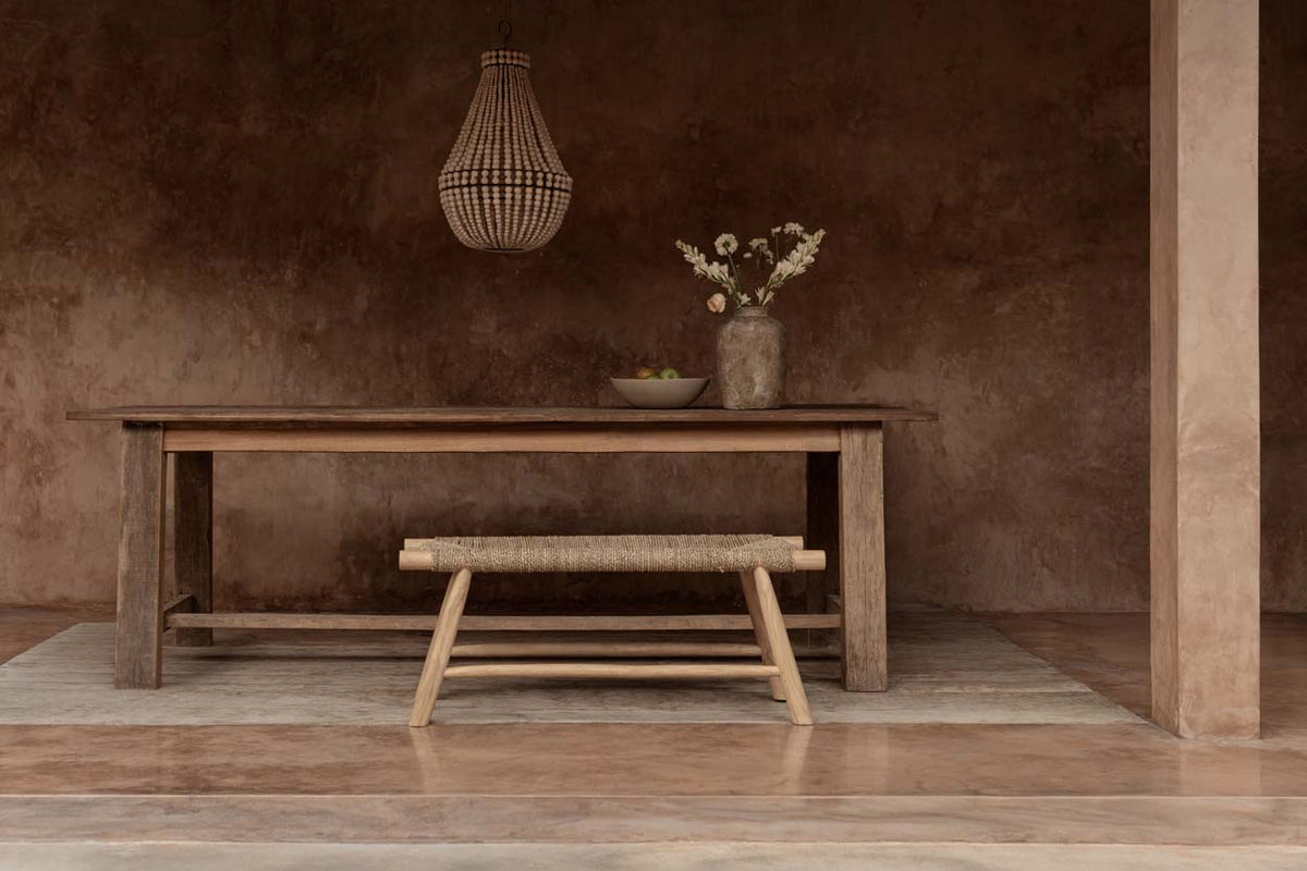 Chandelier with beads above wooden dining table with a bench against a brown wall