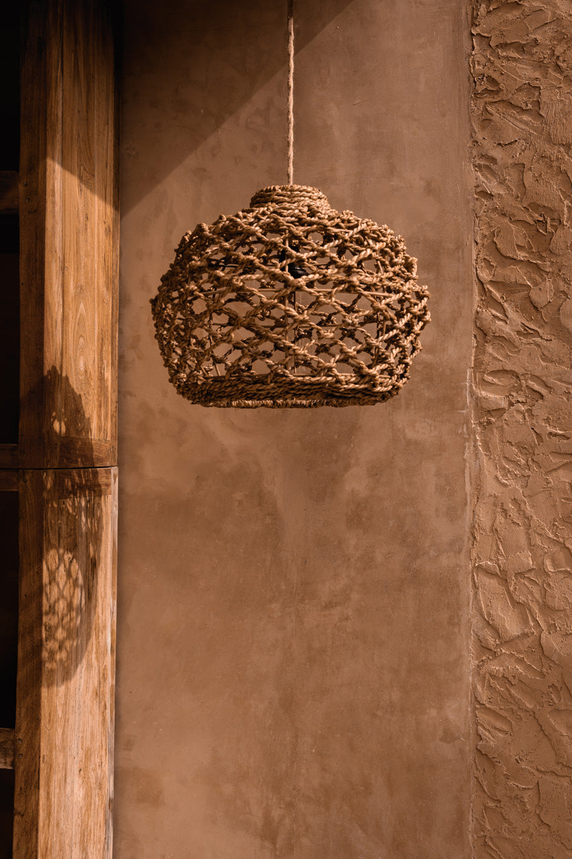 Woven pendant light hanging against a textured wall.