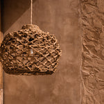 Woven pendant light hanging against a textured  terracotta plastered wall.