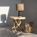 Wooden side table with a woven lamp and bag against a gray wall